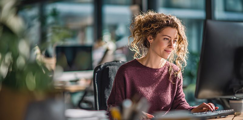 Femme travaillant sur ordinateur dans un bureau lumineux.